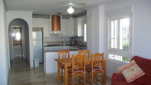 Cozinha espaçosa com armários brancos, uma mesa de jantar com cadeiras e um sofá vermelho na sala de estar.