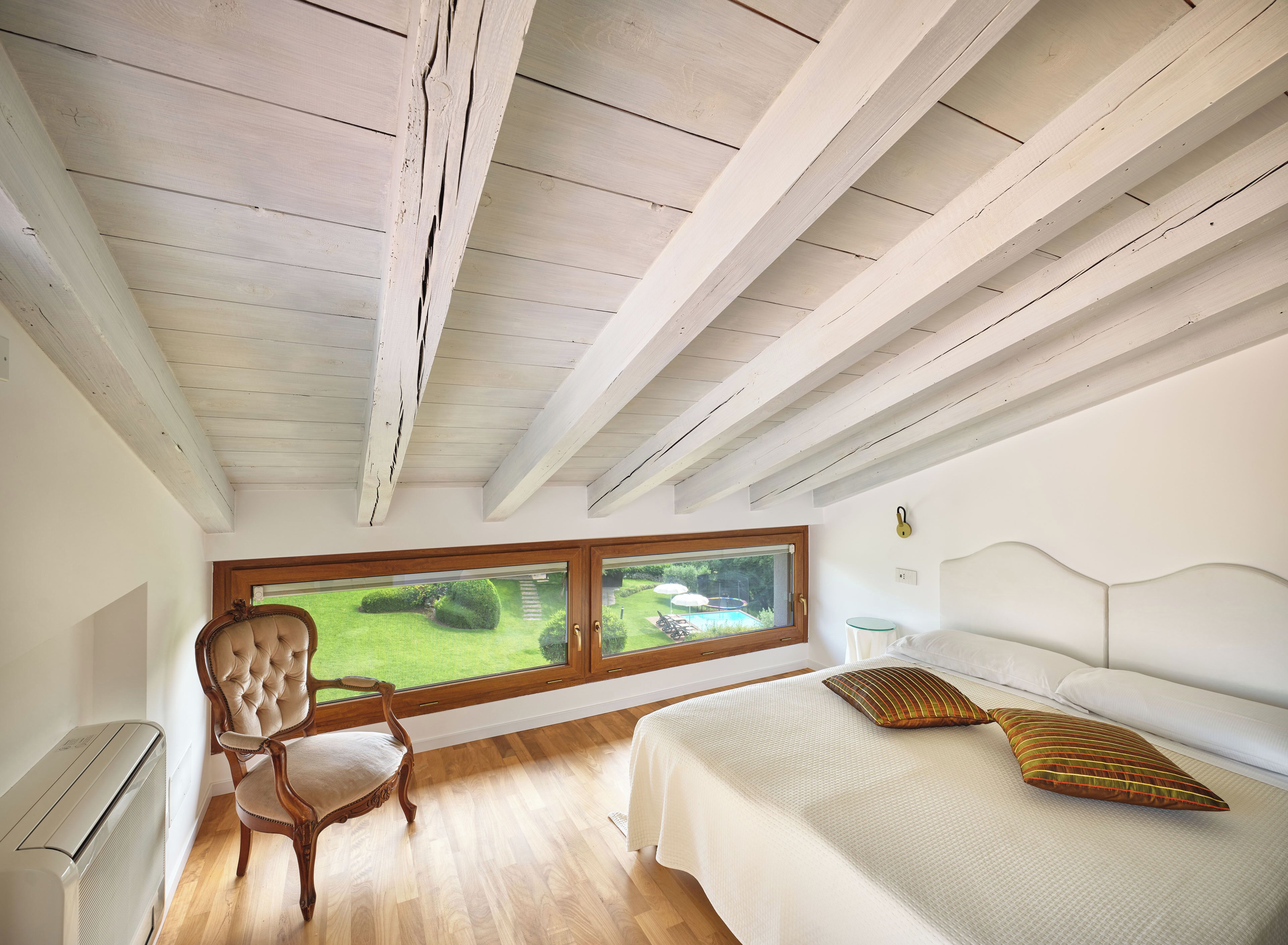 Une chambre avec une grande fenêtre, un lit, une chaise et un radiateur.