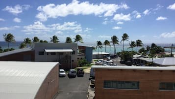 A view of a parking area with several cars, a building with a flat roof, and palm trees in the background.