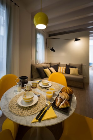 Enjoy a warm breakfast at the round table, set with a coffee pot, cups, plates, and a croissant.