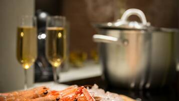 A wooden cutting board with cooked shrimp and ice, a pot, and two glasses of champagne in the background.
