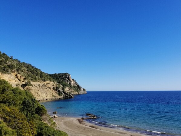 A coastal landscape with a beach, rocky cliffs, and a clear blue sky. - Can Xicu d´es Falcóns (Ibiza)