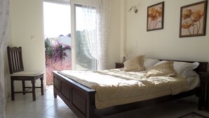 Un dormitori amb llit, cadira, tauleta de nit, làmpada i dos quadres florals emmarcades a la paret.