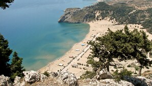Paisatge costaner amb platja, terreny rocos i vegetació escassa.