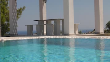 Relax by the serene pool surrounded by pillars and a pergola, with a view of the ocean in the distance.