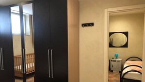 Et soveværelse med seng, tremmeseng, garderobe, natbord med lampe og et spejl på væggen.
