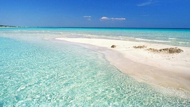 Een strand met helder turquoise water en een zandstrand.