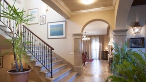 Un grand escalier, avec un pot de plantes sur le côté gauche, mène à un couloir dont les murs sont ornés d’œuvres d’art encadrées.