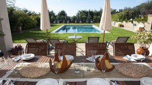 Un espace extérieur aménagé pour les repas, avec vue sur une piscine, entouré de chaises longues et de parasols.