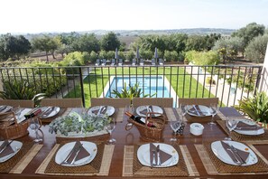 Un espace repas offrant une vue sur une piscine et un jardin aménagé.
