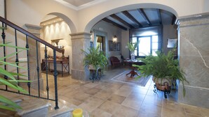 Un hall d’entrée spacieux, agrémenté d’un grand escalier, de grands pots de plantes et d’un plafond haut avec des poutres apparentes.