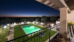 Vue nocturne d’un espace piscine, avec un ciel dégagé, une pelouse bien entretenue et un balcon doté d’une balustrade.