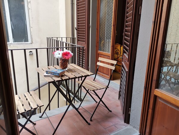 A small balcony with a wooden table, a chair, and a vase with flowers.