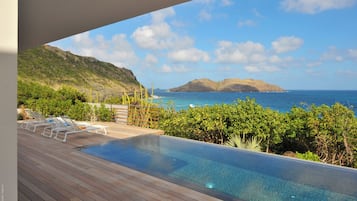 A pool with lounge chairs and a view of the ocean.