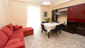 A living room with a red sofa, a dining table with chairs, a kitchen area with cabinets, and a tiled floor. - Cosy apartment, near Metro A, S. Pietro and the downtown (Roma)