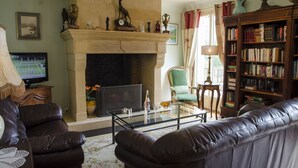 A living room with a fireplace, leather sofas, a glass coffee table, a bookshelf, and a television.