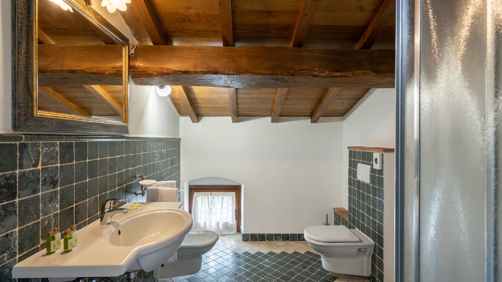 A bathroom with a bathtub, sink, and toilet. The walls are tiled, and there is a wooden ceiling.