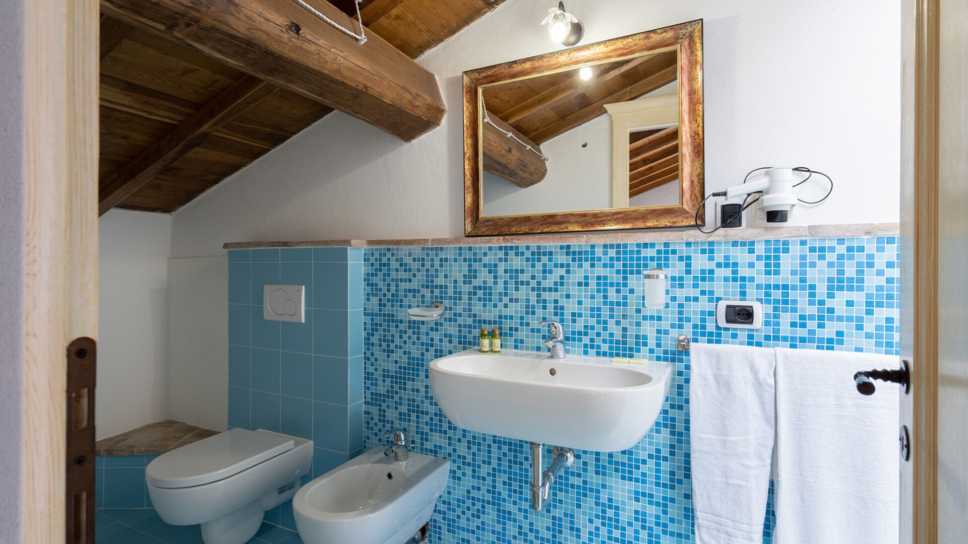Une salle de bain avec un lavabo blanc, un bidet et des toilettes. Un miroir est placé au-dessus du lavabo et une serviette est accrochée au mur.