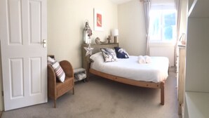 A bedroom with a single bed, a chair, a nightstand, and a window with curtains.