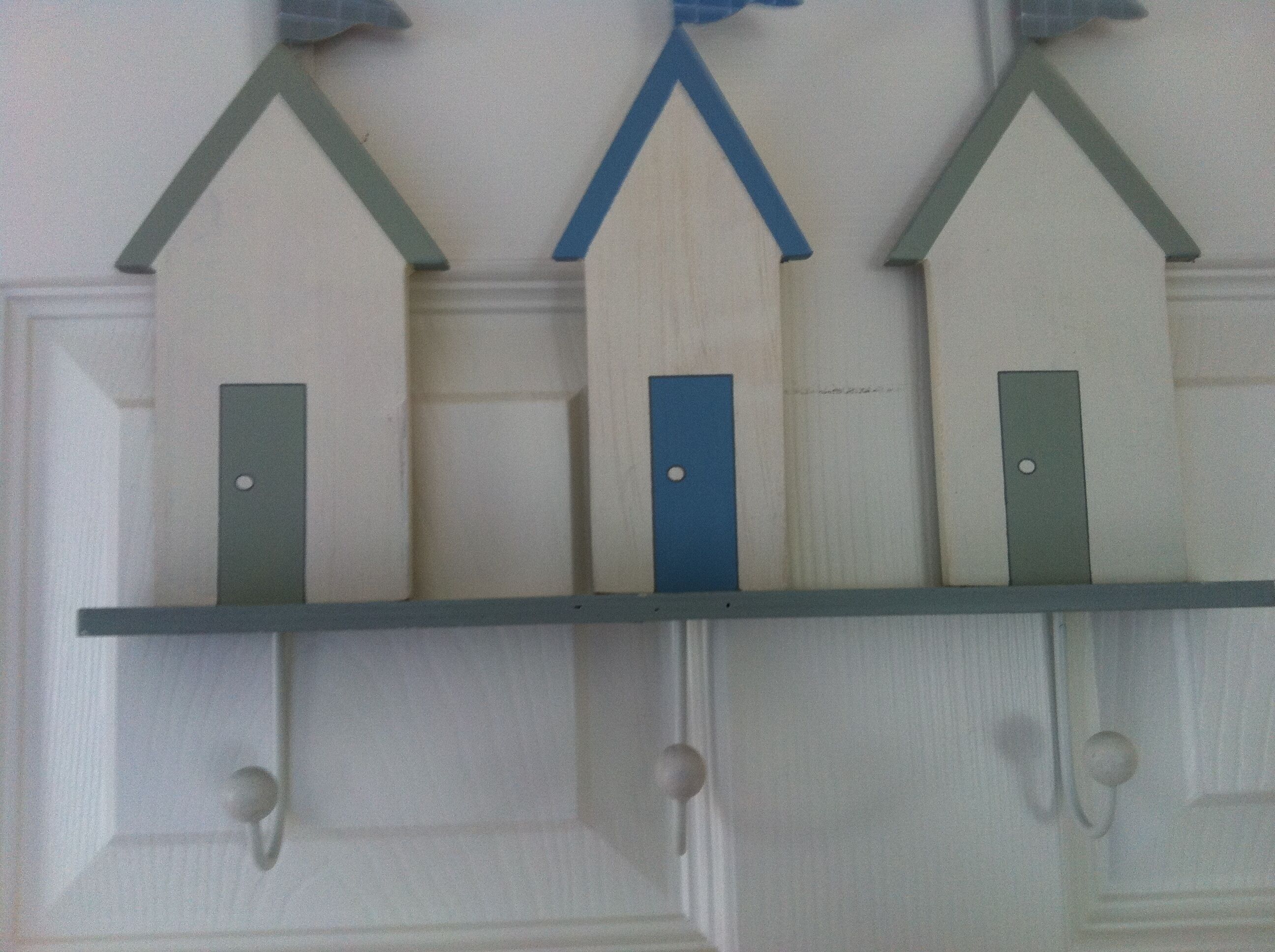 A wall-mounted shelf with three wooden houses, each with a door.