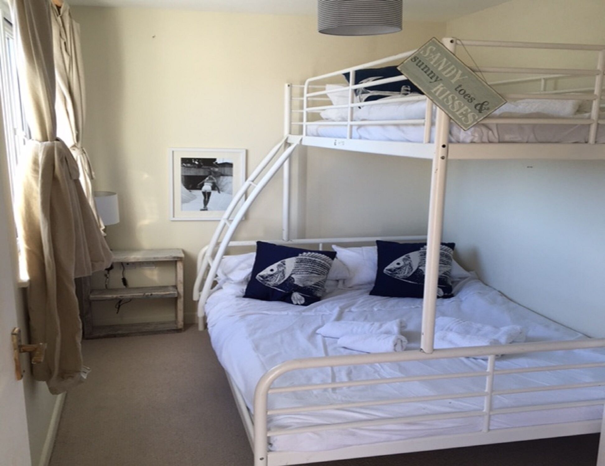 Een slaapkamer met een stapelbed, een bordje op het bovenste bed, een ingelijst foto aan de muur, en een nachtkastje met een lamp.