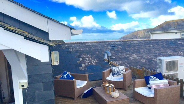 A rooftop patio with wicker furniture, a white air conditioning unit, and a view of the sea.