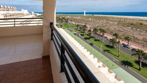 A balcony with a view of a beach, a lighthouse, and a road with palm trees.