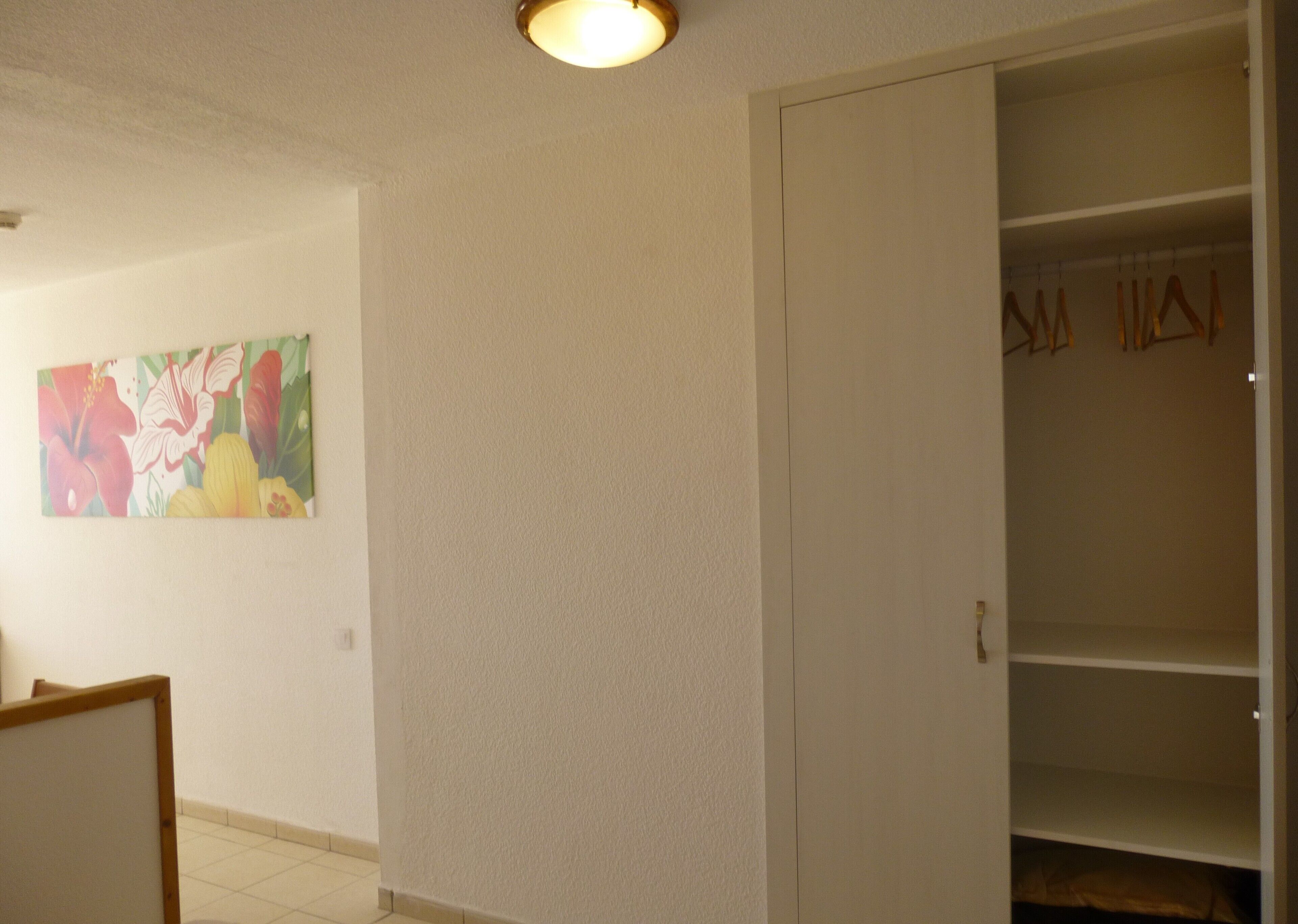 Una habitación con una pared blanca, una puerta con espejo y una lámpara en el techo.
