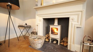 A room with a white fireplace, a standing lamp, a wicker basket, and a metal rack with candles. - Hot tub, beautifully restored Manse. Fantastic midweek rates available. (Stanley)