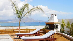 A wooden deck with two lounge chairs and a palm tree, overlooking a beach and mountains. - Detached Villa with Panoramic Sea Views in Beautiful Vlicha Bay, Lindos, Rhodes (Rhodes Island)