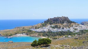 A coastal town with a prominent castle on a hill, a harbor with boats, and a mix of residential and commercial buildings. - Detached Villa with Panoramic Sea Views in Beautiful Vlicha Bay, Lindos, Rhodes (Rhodes Island)