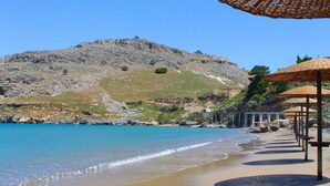A beach with umbrellas and a rocky hillside in the background. - Detached Villa with Panoramic Sea Views in Beautiful Vlicha Bay, Lindos, Rhodes (Rhodes Island)