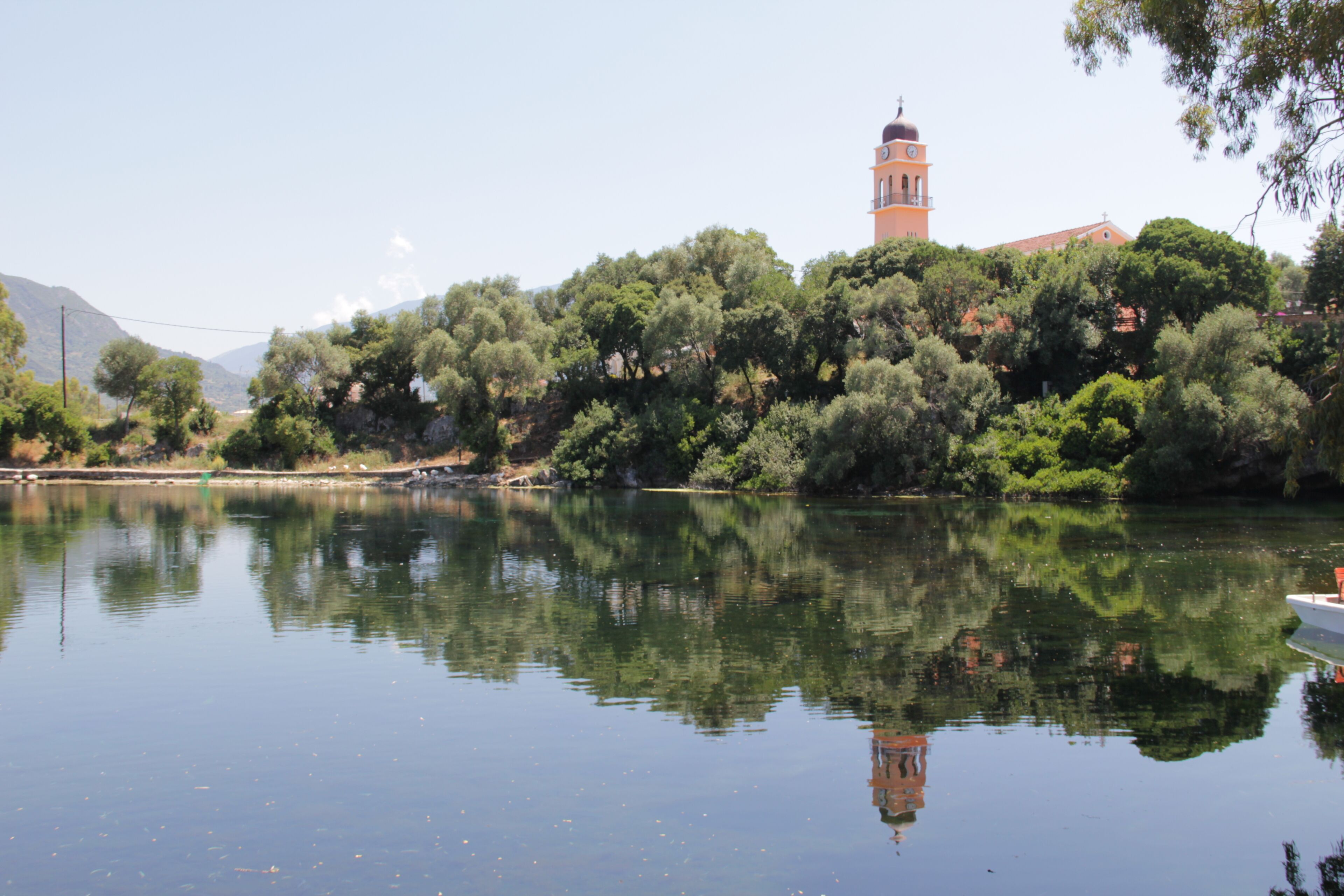 A calm lake with a reflection of trees and a building with a bell tower.