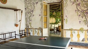 Une table de ping-pong dans une pièce dont un mur est décoré d’une fresque florale, avec un banc en bois et une lampe suspendue.
