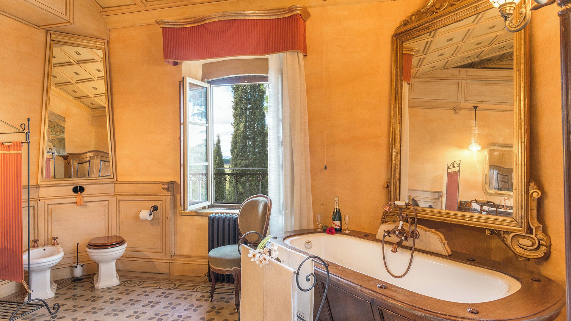 A classic bathroom with a freestanding bathtub, a large mirror, and a window with a view of trees.