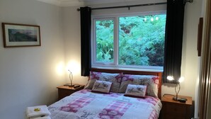 Une chambre à coucher comprenant un lit, deux tables de chevet, une commode, une fenêtre avec des rideaux et un tableau encadré accroché au mur.