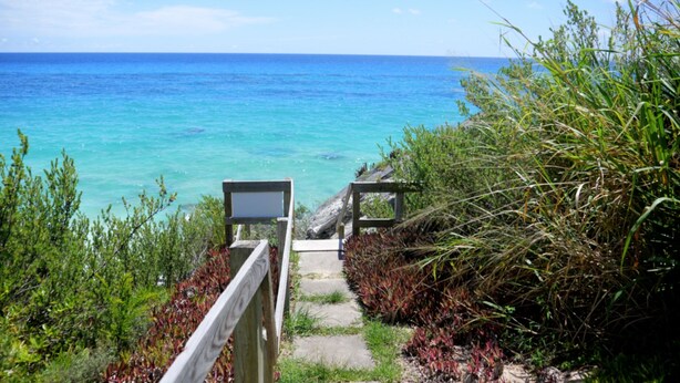 Un sentier en bois mène à une plage bordée d’une eau turquoise et cristalline.