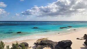 Une plage aux eaux turquoise et limpides, bordée de rochers et d’une étendue de sable.