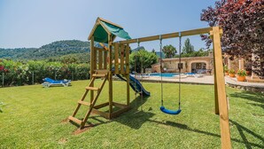 Ein Spielplatz mit Schaukeln, einer Rutsche, einem Pool und einer Hügelkulisse im Hintergrund.