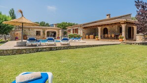 Eine Steinvilla mit Swimmingpool, Sitzgelegenheiten im Freien und einem gepflegten Rasen.