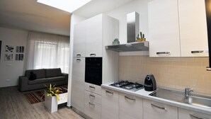 A compact kitchen with a gas stove, a built-in oven, and a sink. There is a sofa and a small table with a plant in the living area. - Elegant house with veranda - in the center of Rome, a stone's throw from S. Giovanni  (Roma)