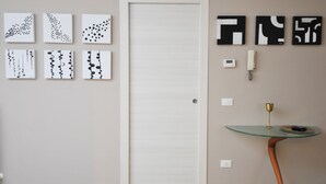 A room with a white door, six wall-mounted artworks, a telephone, and a small glass table with a gold cup. - Elegant house with veranda - in the center of Rome, a stone's throw from S. Giovanni  (Roma)