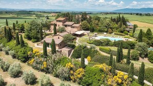A villa with a swimming pool surrounded by lush gardens and tall cypress trees.