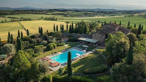 An aerial view of a property with a swimming pool, surrounded by lush greenery and a large house with a patio area.