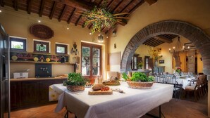 A rustic dining area with a table set for a meal, surrounded by wooden beams and brick arches.