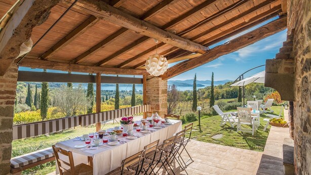 Un área de comedor al aire libre con una mesa preparada para cuatro personas, con vistas a un paisaje pintoresco con árboles y montañas.