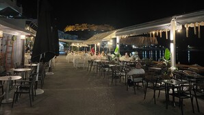 Un espace extérieur aménagé pour les repas, avec des tables et des chaises, une vue sur la mer et un bâtiment en arrière-plan.
