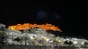 Une ville côtière de nuit, avec des bâtiments illuminés et une colline bien visible.