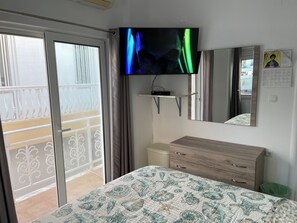 A hotel room with a bed, a TV mounted on the wall, a dresser, and a balcony with a railing.