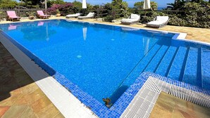 Una piscina cristallina blu con lettini e ombrelloni, immersa nel verde e delimitata da una recinzione in legno.